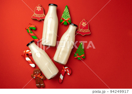 Glass milk bottle and Christmas gingerbread cookies on red background 94249917