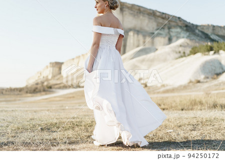 Back view of a bride in a white dress with bare shoulders standing in a field 94250172