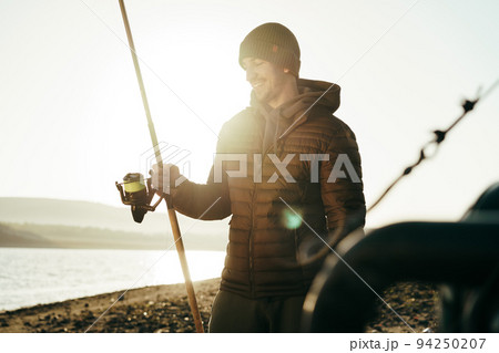 Male fisherman fishing at the lake at sunrise Male fisherman fishing at the lake at sunrise 94250207
