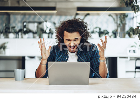 Stressed and disappointed young man freelancer looking at his laptop, got bad news Stressed and disappointed young man freelancer looking at his laptop, got bad news 94250434