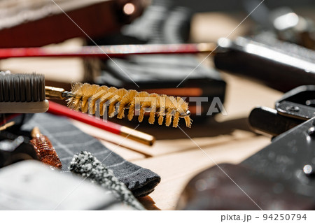 Black disassembled shotgun and cleaning tools on wooden table . 94250794