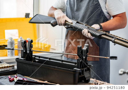 Close up of young man in apron disassembling a gun above the table 94251180