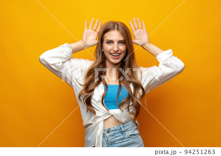 Young woman standing over yellow background doing funny gesture with hands over head as horns Young woman standing over yellow background doing funny gesture with hands over head as horns 94251263
