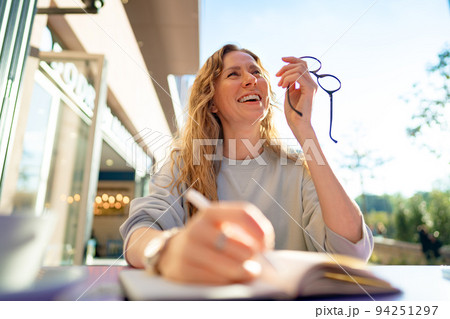 Casual woman sitting at table and taking notes in notebook .on the cafe terrace Casual woman sitting at table and taking notes in notebook .on the cafe terrace 94251297
