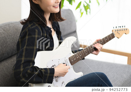ソファに座りギターを弾く女性 ソファに座りギターを弾く女性 94252773