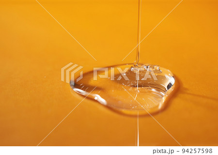 A drop of body gel or shampoo pouring from above on a yellow saturated background. 94257598