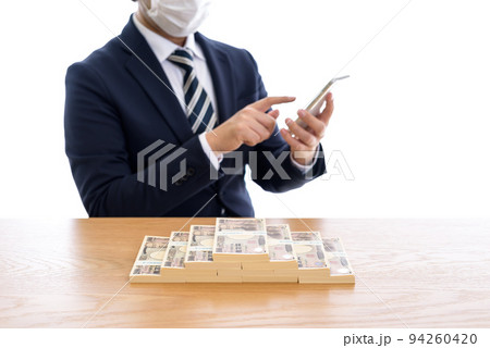 百万円を並べた一千万円を前にスマホを操作するビジネスマン　日本円 94260420