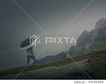 Rear view of a lonely man with umbrella stands on a rocky hill covered by haze. Moody and emotional scene with a lone stranger silhouette under the rain Rear view of a lonely man with umbrella stands on a rocky hill covered by haze. Moody and emotional scene with a lone stranger silhouette under the rain 94260908