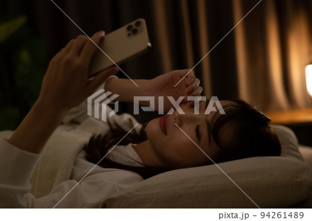 ベッド・寝室で目を擦りながらスマホを操作する女性 94261489