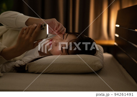 ベッド・寝室で目を擦りながらスマホを操作する女性 94261491