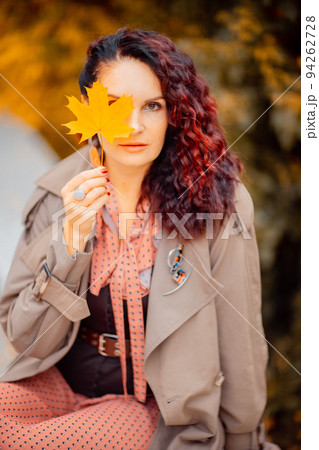 Beautiful girl walking outdoors in autumn. Smiling girl collects yellow leaves in autumn. Young woman enjoying autumn weather. 94262728