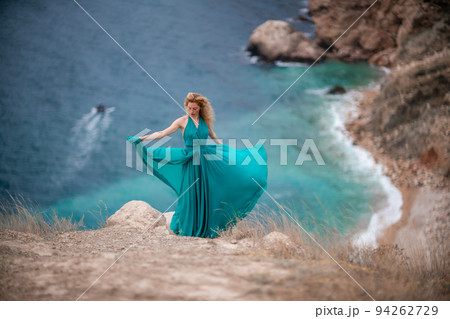A woman in an emerald dress, a fashion model with long silk wings in a flowing dress, flying fabric on the embankment. 94262729