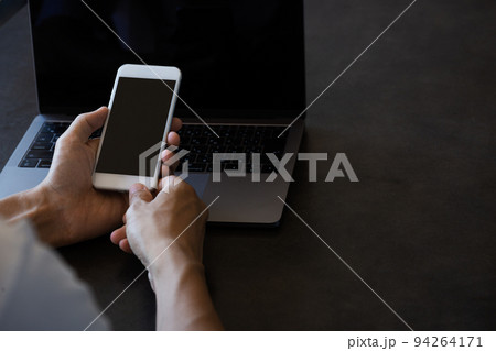 ノートパソコンの前でスマートフォンを操作する男性 ノートパソコンの前でスマートフォンを操作する男性 94264171