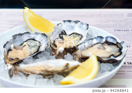 Opened oysters and lemon with white wine on the table. Restaurant delicacy, simple table setting. Saltwater oysters dish. Romantic dinner in restaurant Opened oysters and lemon with white wine on the table. Restaurant delicacy, simple table setting. Saltwater oysters dish. Romantic dinner in restaurant 94268841