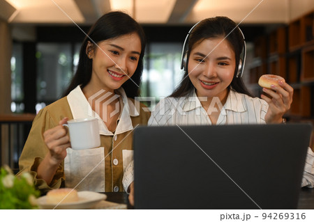 Two smiling women preparing for exams, learning together in modern college library. Education, people and technology concept Two smiling women preparing for exams, learning together in modern college library. Education, people and technology concept 94269316