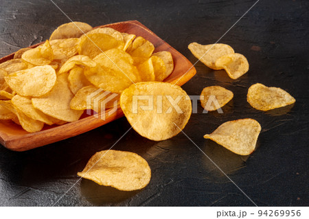 Potato chips or crisps in a bowl and scattered on a black stone background Potato chips or crisps in a bowl and scattered on a black stone background 94269956