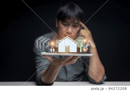 Tablet in hand of a man contemplating buying his first home with a preview of the house displayed above the tablet screen. first home buying idea. selective focus on tablet. Tablet in hand of a man contemplating buying his first home with a preview of the house displayed above the tablet screen. first home buying idea. selective focus on tablet. 94272208