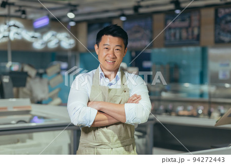 portrait of handsome asian man salesman in apron standing and looking at camera in grocery store supermarket. Male worker seller or small business owner. indoor. food, groceries market Cheerful smile 94272443