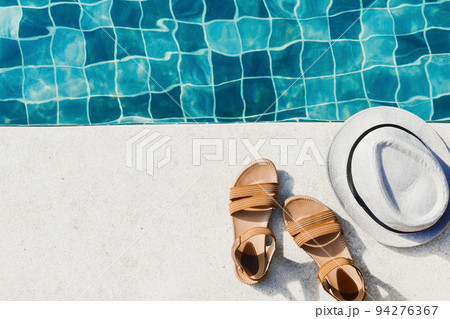 Vacation flat lay with woman's sandals and hat front of the pool 94276367