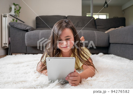 Adorable little girl using a digital tablet on the floor at home. 94276582