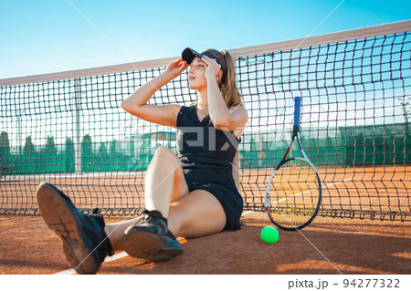Portrait of a woman on the court. Tennis stadium, athlete with racket and ball. Sports grid. The girl rests after training. Active lifestyle, outdoor. Sunny day, summer. sunset. Smiles, happiness Portrait of a woman on the court. Tennis stadium, athlete with racket and ball. Sports grid. The girl rests after training. Active lifestyle, outdoor. Sunny day, summer. sunset. Smiles, happiness 94277322