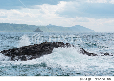 coastal seascape, rocks in the surf against the backdrop of a distant wooded shore 94278160