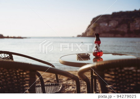 empty cafe table and chairs on sandy beach with ashtray and candle light in front of sea golf with clear sky before sunset 94279025