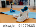 White sports sneakers with laces on the yellow floor. Next to it is a yoga mat and two small blue dumbbells. Everything you need for fitness. 94279883