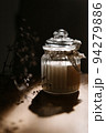 The vanilla candle is tied with a vintage ribbon. Bright sun rays pass through the transparent glass. A blurry gypsophila branch in the background. 94279886