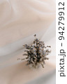 A dried lavender branch in close-up on a white flowing fabric. The background is blurred. Top view 94279912