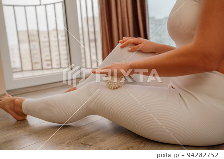 Athletic slim caucasian woman doing thigh self-massage with a massage ball indoors. Self-isolating massage 94282752