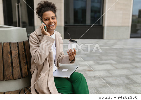 young african american woman sitting near the business center during lunch break with a laptop and a 94282930