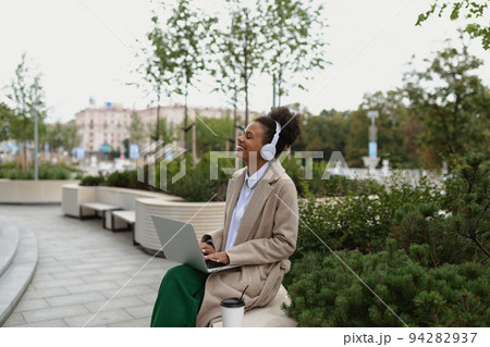 a young black student with a laptop sitting on a bench listening to music in headphones with a young black student with a laptop sitting on a bench listening to music in headphones with 94282937