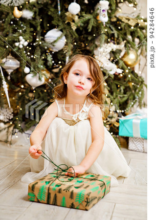 little girl with box of gift by Christmas tree. tradition giving gifts 94284646