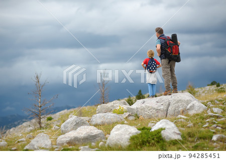 Cute schoolchild and mature father hiking together on mountain and exploring nature. Child learning survival skills and orienteering. Concepts of adventure, scouting and hiking tourism for kids. 94285451