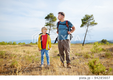 Cute schoolchild and his mature father hiking together on mountain and exploring nature. Concepts of adventure, scouting and hiking tourism for kids. 94285607