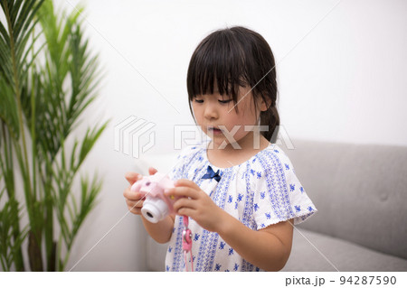 自宅の部屋でおもちゃのカメラを撮って遊ぶ女の子 94287590