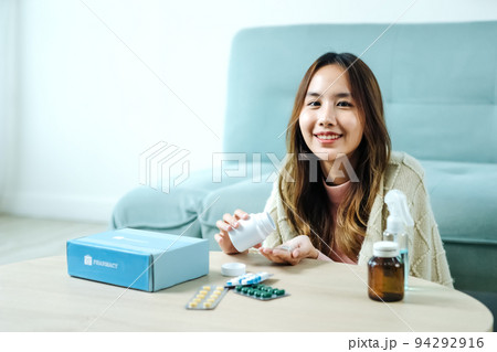 Young Asian woman sick, tired, she sitting and resting on blue fabric sofa and blanket after takes medicines pills in living room at her home. Woman use the phamacy first aid kit box from delivery Young Asian woman sick, tired, she sitting and resting on blue fabric sofa and blanket after takes medicines pills in living room at her home. Woman use the phamacy first aid kit box from delivery 94292916