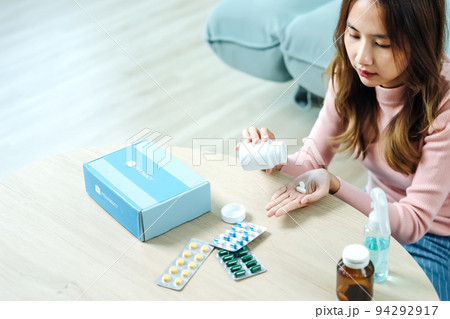 Young Asian woman sick, tired, she sitting and resting on blue fabric sofa and blanket after takes medicines pills in living room at her home. Woman use the phamacy first aid kit box from delivery Young Asian woman sick, tired, she sitting and resting on blue fabric sofa and blanket after takes medicines pills in living room at her home. Woman use the phamacy first aid kit box from delivery 94292917