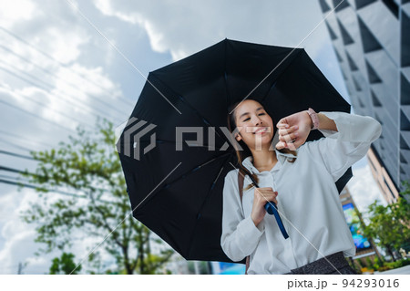 Cute Asian business woman with holding black umbrella looking at watch outdoors on sunny day, focus to the watch 94293016