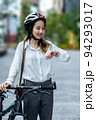 Young Asian businesswoman wearing helmet and standing on a city street with bicycle looking at the watch. 94293017