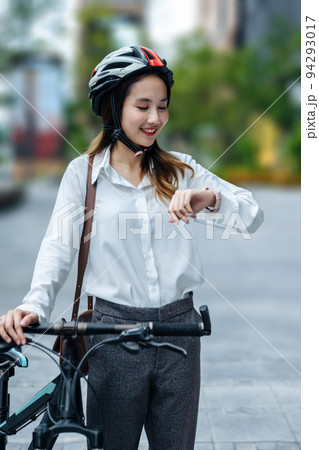 Young Asian businesswoman wearing helmet and standing on a city street with bicycle looking at the watch. 94293017