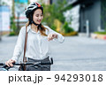 Young Asian businesswoman wearing helmet and standing on a city street with bicycle looking at sky or watch. 94293018