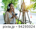 Beautiful Asian woman listening favourite music on headphones from mobile phone, Happiness relaxation summer in park with music riding bicycle in green park. 94293024