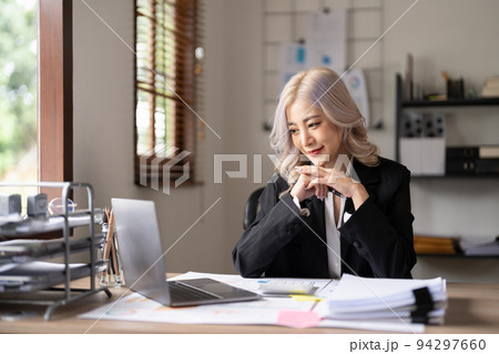 Young finance market analyst working at sunny office on laptop while sitting at wooden table. Businesswoman analyze document graphs and diagramm on notebook screen 94297660