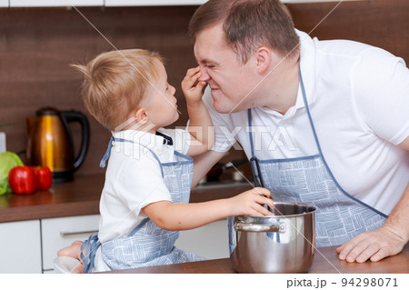 Boy and his father are preparing soup together in kitchen at home. Having fun 94298071