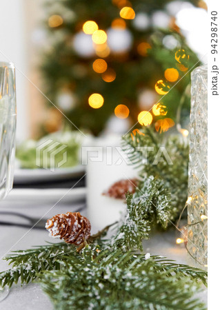 Festive Christmas decorations a pine branch with cones decorate the dinner table Festive Christmas decorations a pine branch with cones decorate the dinner table 94298740