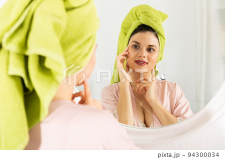 Woman with towel on his head near mirror and touching face 94300034