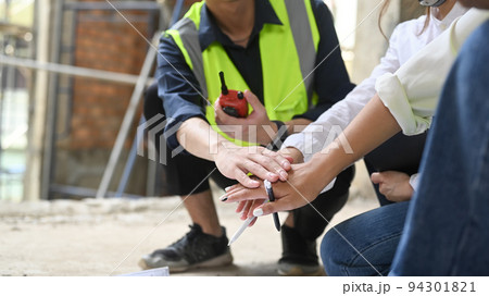 Cropped image of engineer and architects sitting in construction site floor and stacking hands together 94301821