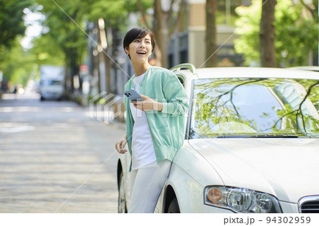 マイカーのそばでスマホを見る若い女性 94302959